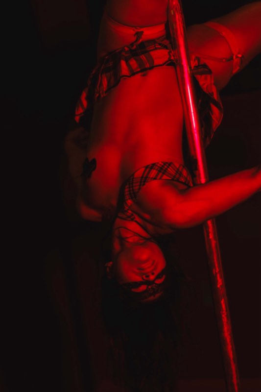 Atuação de pole dance no palco, em luz vermelha