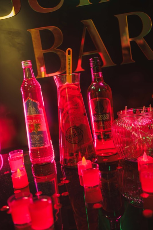 Garrafas iluminadas por luz néon vermelha ao balcão, com velas